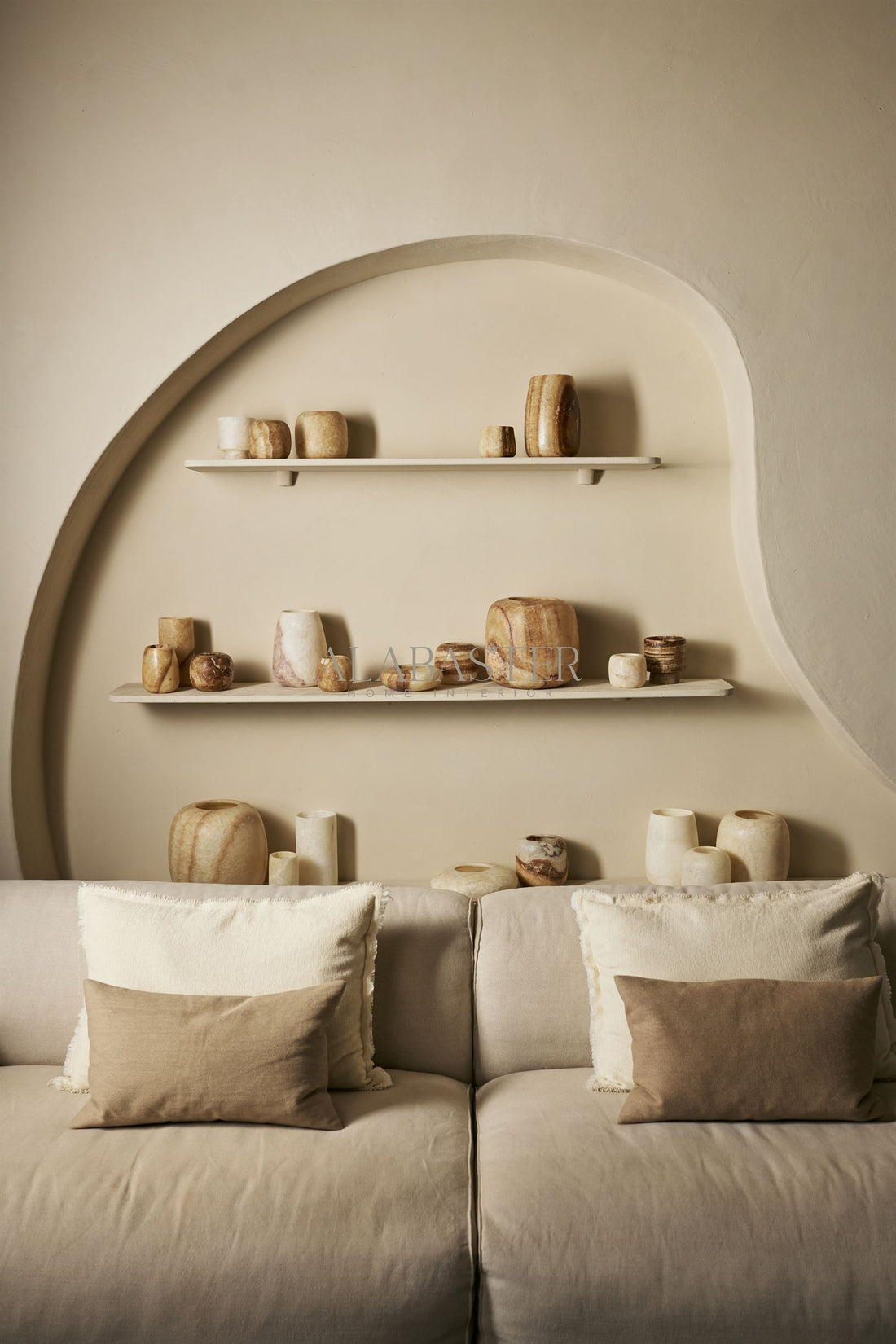 Verzameling handgemaakte alabaster waxinelichthouders in wit en bruin naast elkaar op wandplanken in een warm interieur